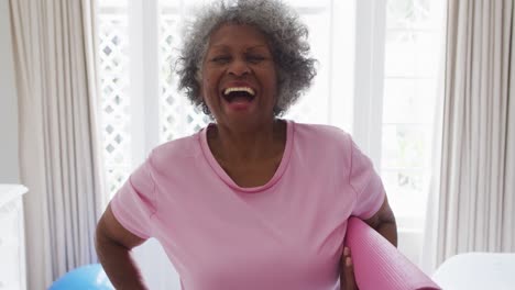 portrait of senior african american woman holding yoga mat smiling at home