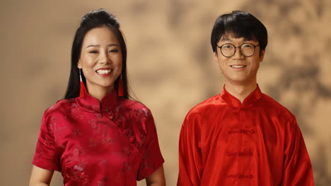 Feliz-Joven-Pareja-Asiática-Con-Ropa-Tradicional-Roja-Mirándose-Y-Sonriendo-Alegremente-A-La-Cámara