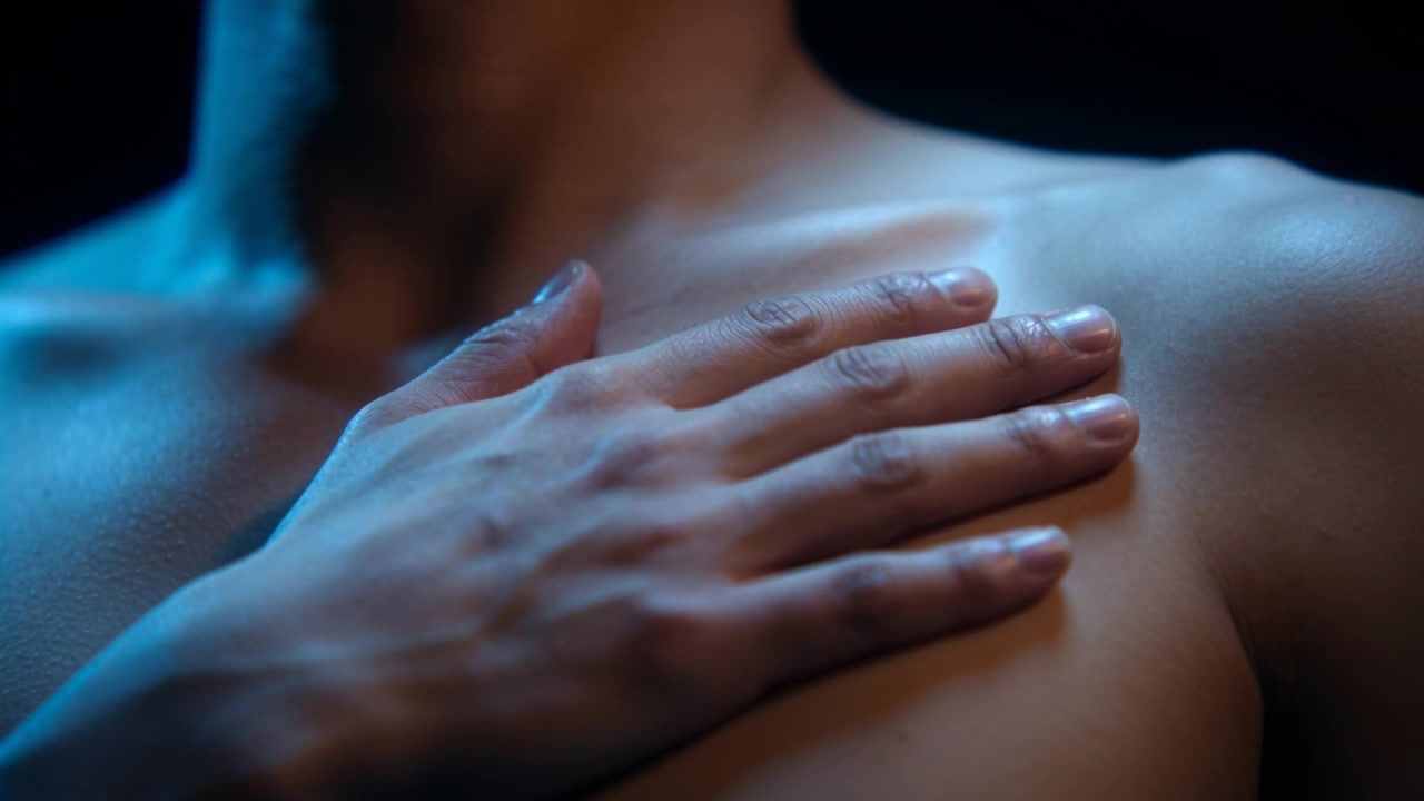 Moving right hand, bare-chested man placing palm over left pectoral in studio, cool blue rim light