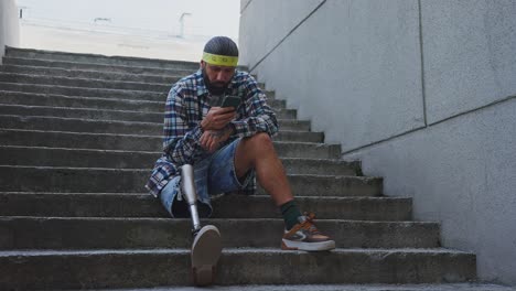 man with prosthetic leg using smartphone on stairs