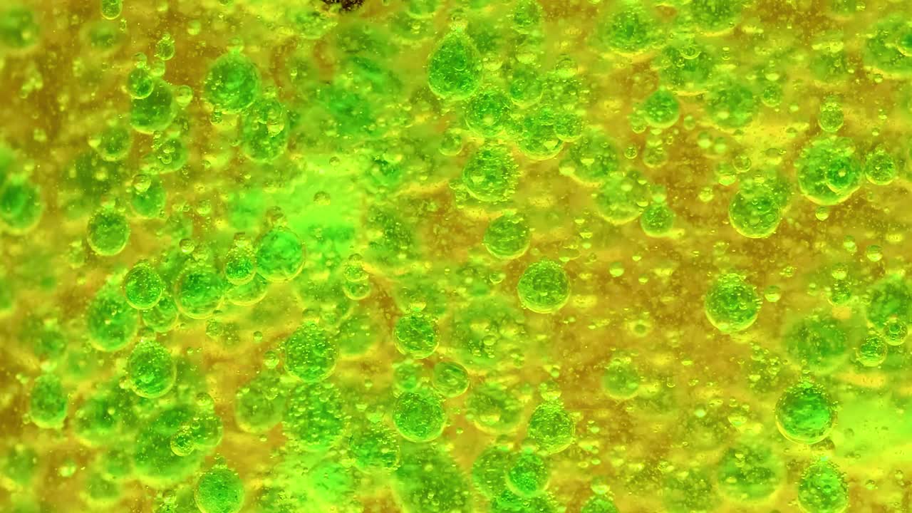 Close-up view of green bubbles floating in a yellow liquid, showcasing dynamic movement and vivid colors.