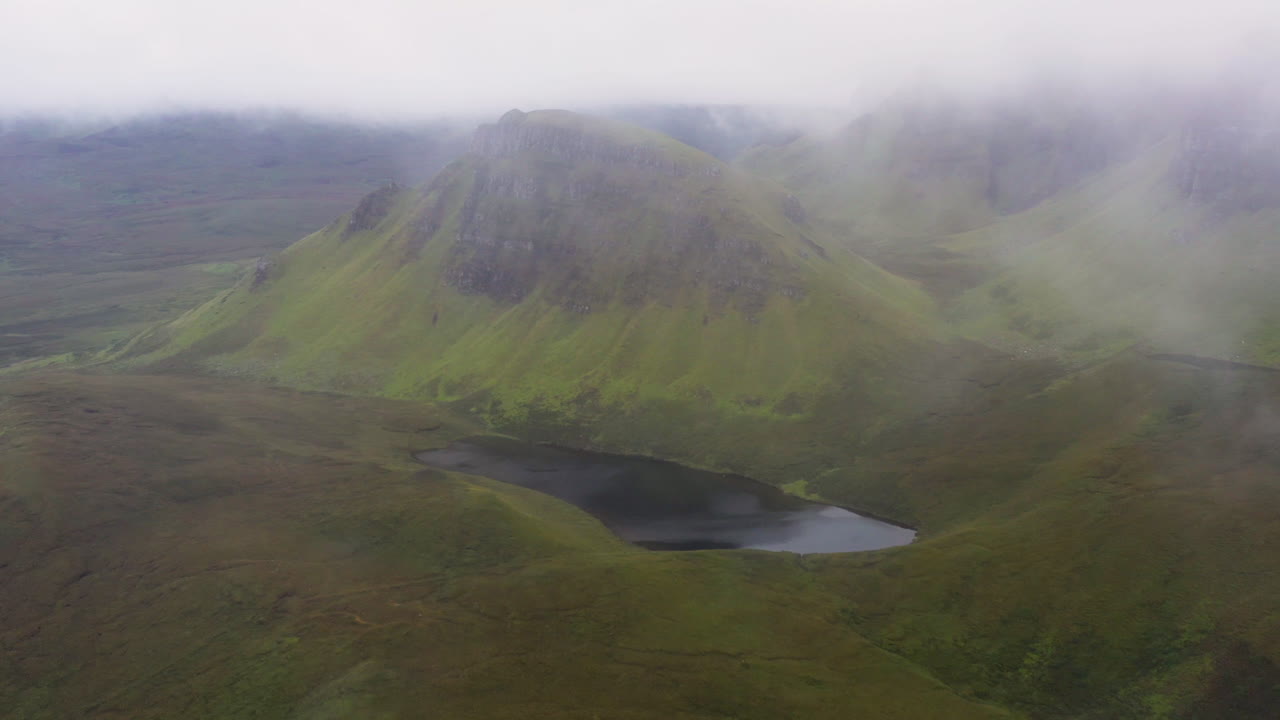 Kinematisk droneopptak som kommer gjennom skyene for å avsløre Quiraing, jordskredet på østsiden av Meall na Suiramach i Skottland