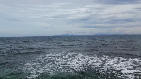 aerial drone shot of foamy waves crashing on reef in middle of vast ocean with cloudy sky in background