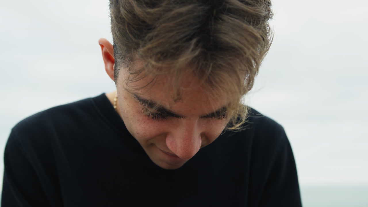 niño nerd jugando juegos de teléfono inteligente sentado en un banco al aire libre cerca del océano