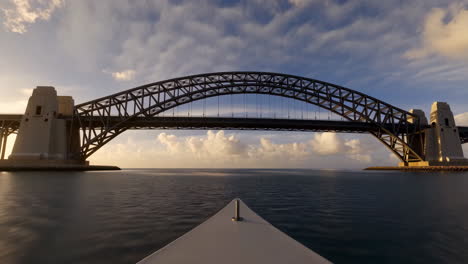 view of a grand arch bridge from a boat on calm waters at sunset