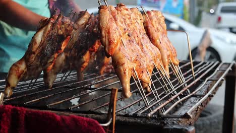 a steady shot of delicious fried chicken grilled on a barbeque by a thai man on the market in thailand