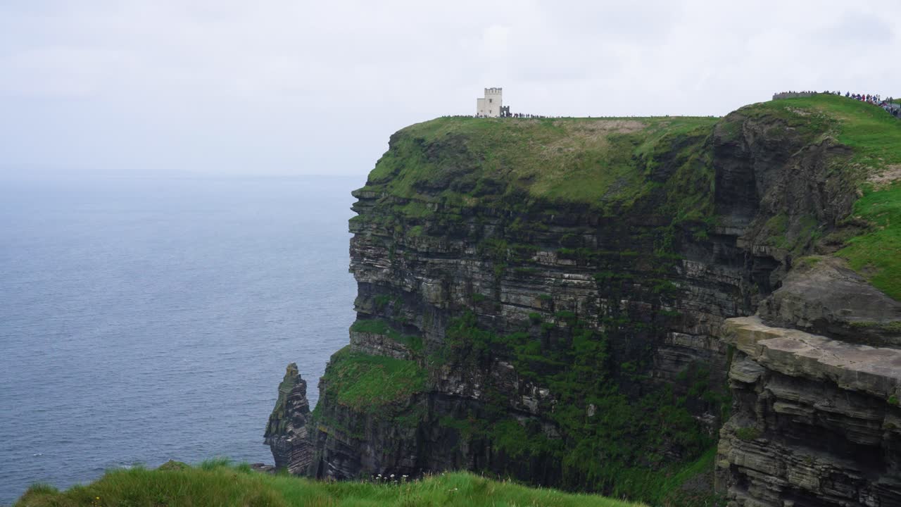 A stunning, wide shot of the world-famous Cliffs of Moher in Ireland. The iconic O'Brien's Tower stands atop the dramatic, green-topped sea cliffs