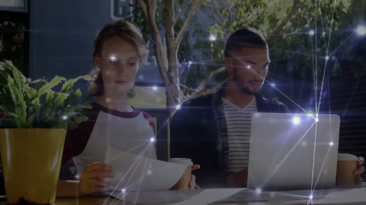 Coworkers sharing laptop and coffee cups on table, displaying glowing technology network nodes