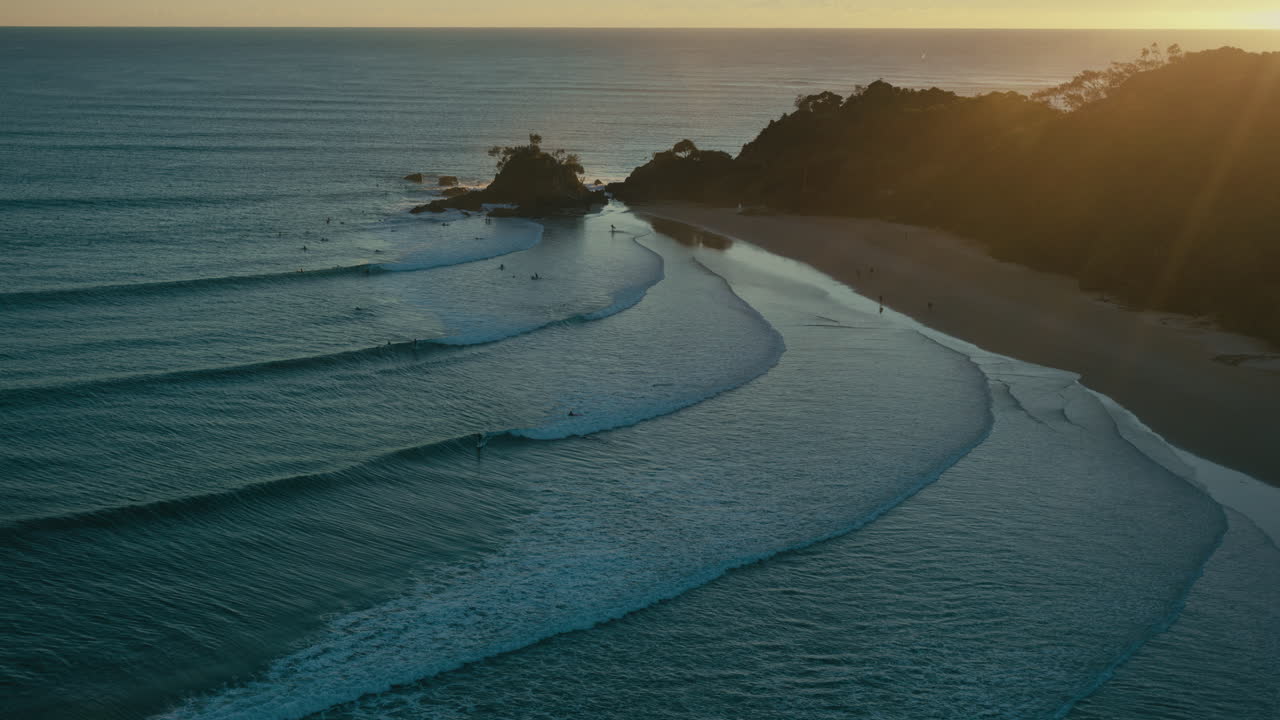Onde che si infrangono dolcemente accarezzano la costa di Byron Bay, mentre la calda luce dell'alba colpisce l'acqua.