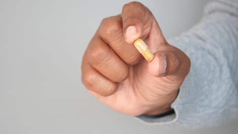 close-up of a hand holding a yellow capsule pill