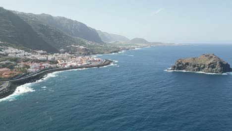 ocean waves roll and crash onto breakwater slopes below picturesque town on tenerife coast