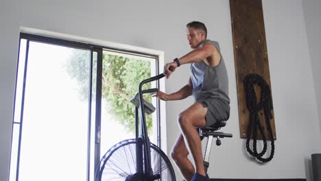 hombre caucásico en forma sudoroso haciendo ejercicio en bicicleta de entrenamiento dentro del gimnasio