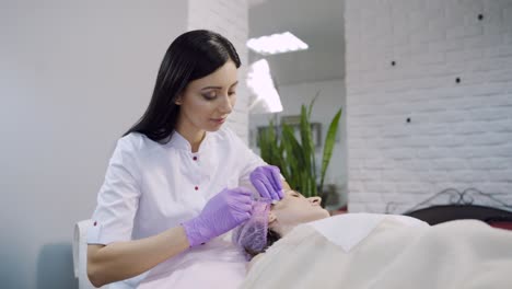 a beautician with long hair checks an injection and starts the biorevitalization procedure on the woman's face. blurred background.