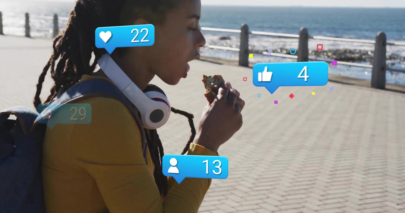 Adult woman lifting sandwich to mouth on seaside promenade causing social media like comment icons