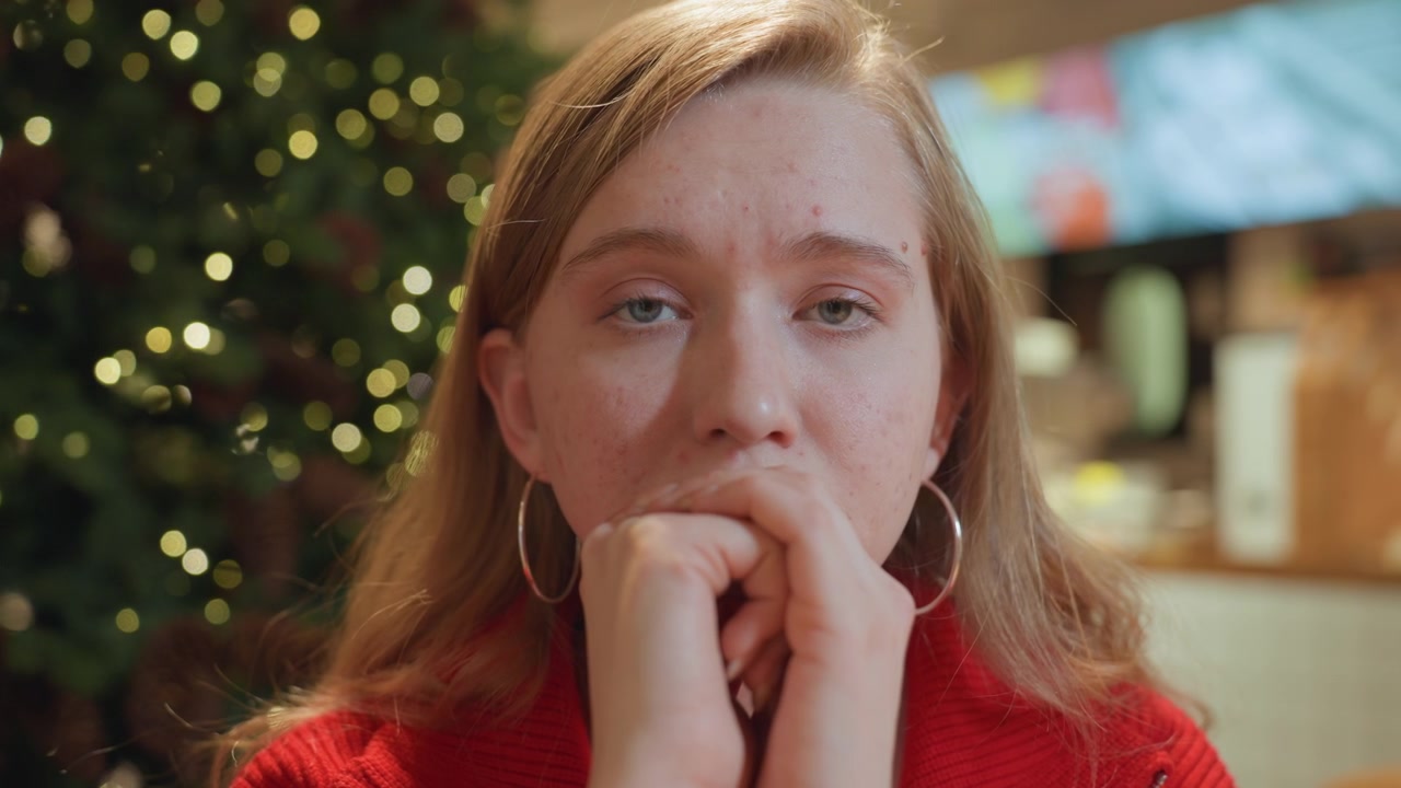 Giovane donna pensierosa che guarda in camera con un albero di Natale sullo sfondo
