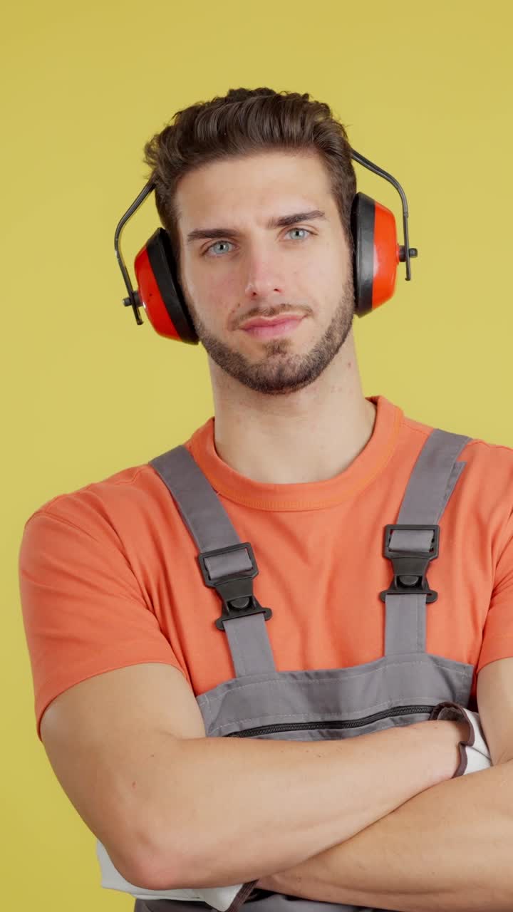 Young Man in Work Overalls and Ear Defenders on Yellow Background