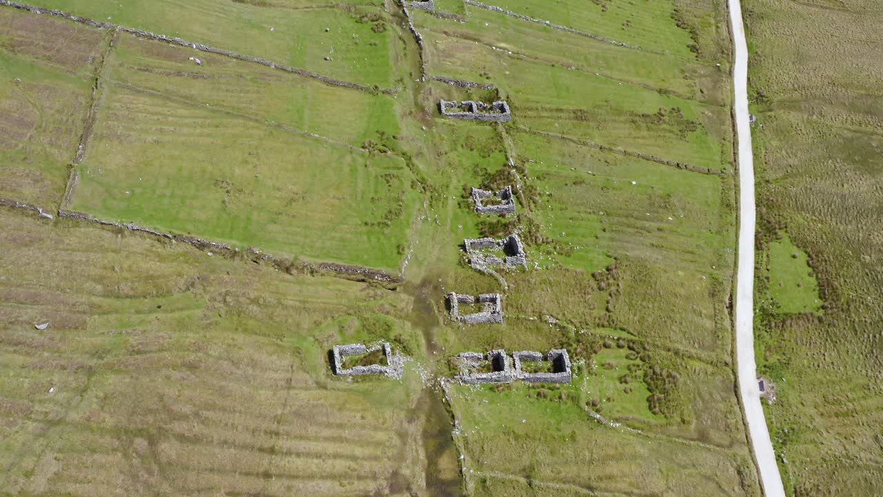Tilt down aerial reveals historic archeological rock wall ruins of old abandoned village at slievemore, ireland