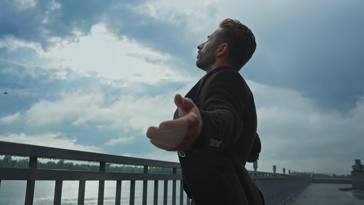 Man in a Brown Jacket by a River on a Cloudy Day