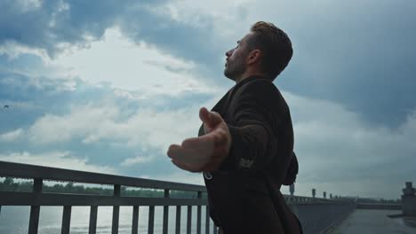 man in a brown jacket by a river on a cloudy day