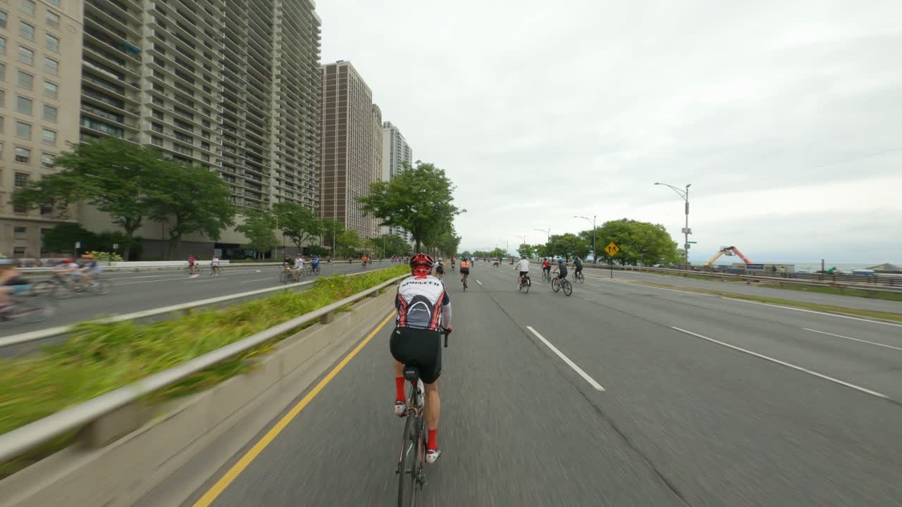 Cyclists riding along a scenic lakefront road with city buildings