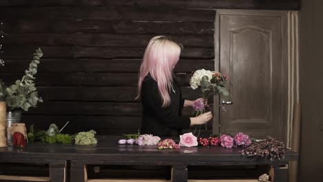 a pretty girl florist on a dark background makes a composition of flowers. modern, wooden interior