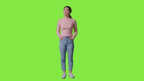 녹색 스크린에 대한 프레임 주위를 보기 위해 회전하는 여성의 전체 길이 스튜디오 초상화
