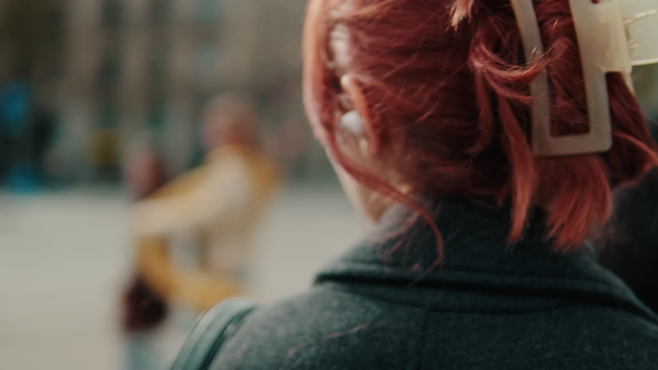Giovane donna con i capelli rossi che ascolta musica con auricolari wireless in città