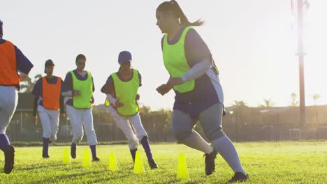 diverse group of female baseball players exercising on pitch, running between cones