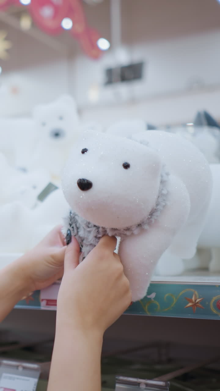 검은 셔츠와 안경을 입은 긴 갈색 머리카락을 가진 미소 짓는 여성의 측면 시각 백색 플러시 북극  장난감과 함께 스카프 상점 선반에 축제 휴가 장식으로 둘러싸여