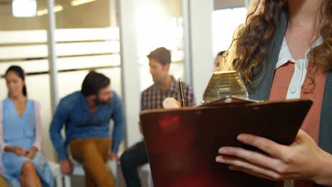 mujer de negocios escribiendo en el clipboard mientras sus colegas discuten en segundo plano