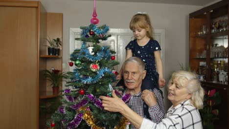 Kleines-Mädchen-Mit-Großmutter-Und-Großvater,-Die-Einen-Künstlichen-Weihnachtsbaum-Mit-Spielzeug-Dekorieren