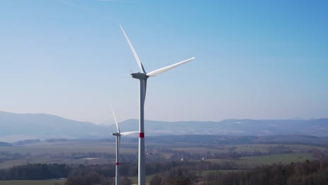 Molinos-De-Viento-En-Campos-Con-Colinas-En-El-Fondo---Toma-Panorámica-En-Cámara-Lenta