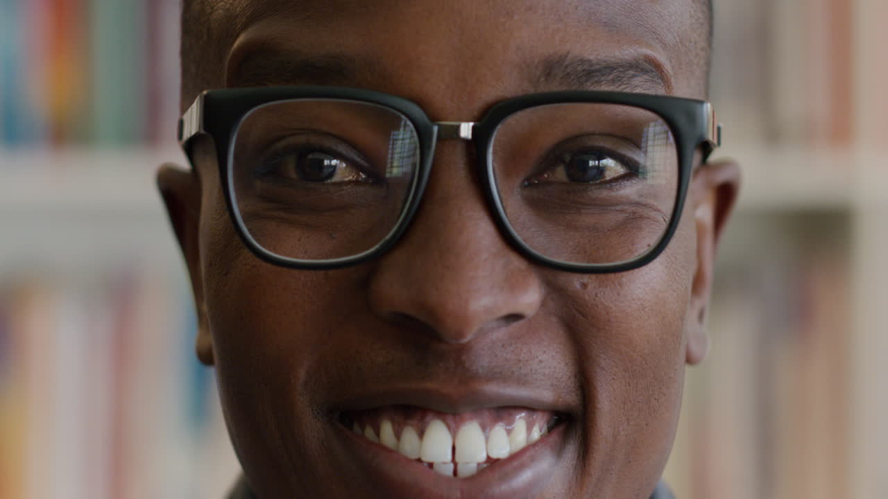 Portræt af glad afroamerikansk mandlig studerende, der smiler foran en bogreol.
