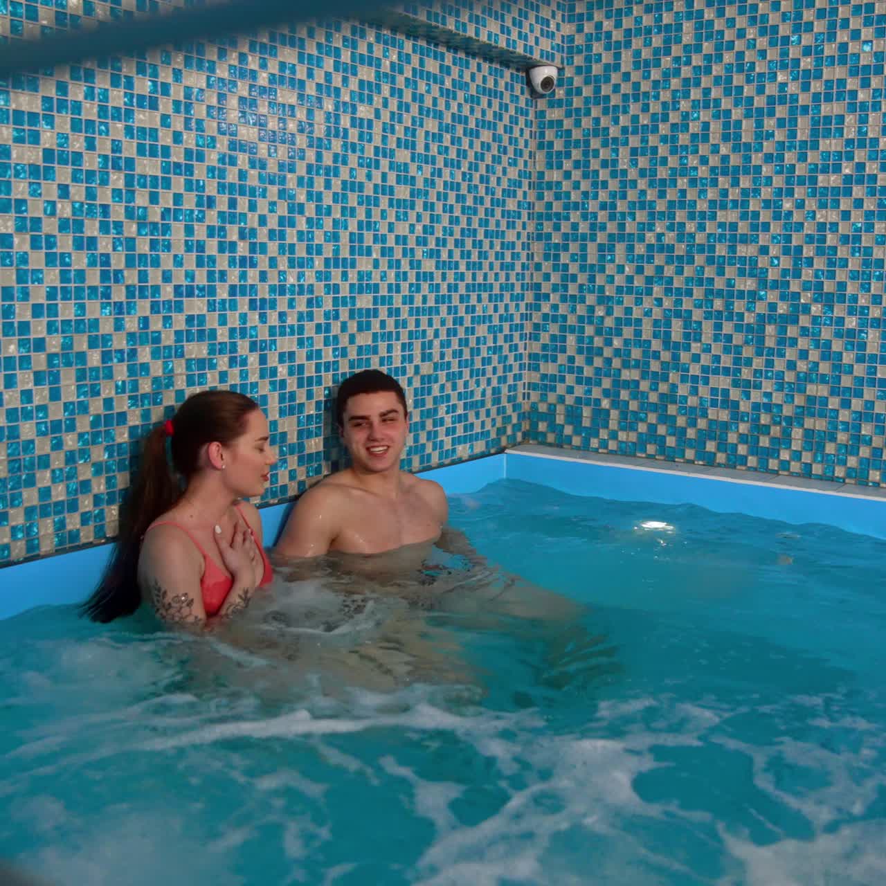 Happy people spending time in the pool indoors. Couple talking and laughing while sitting in the jacuzzi. Spa centre relaxation