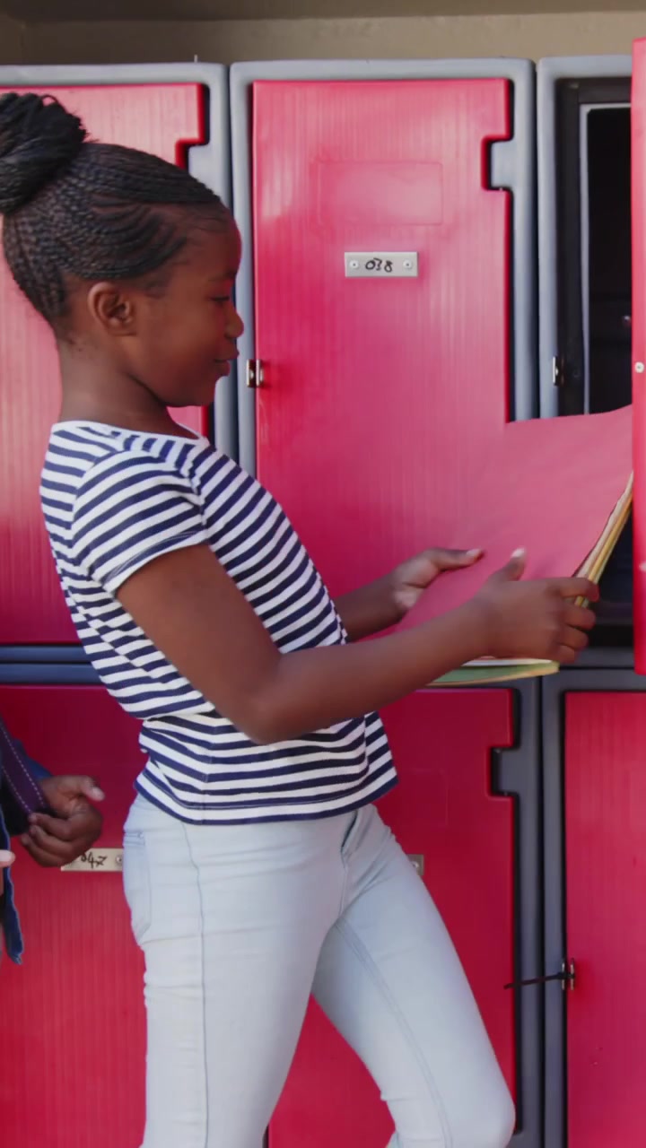 Vertical video: African American schoolgirls walking to locker, girl opening it, getting folders