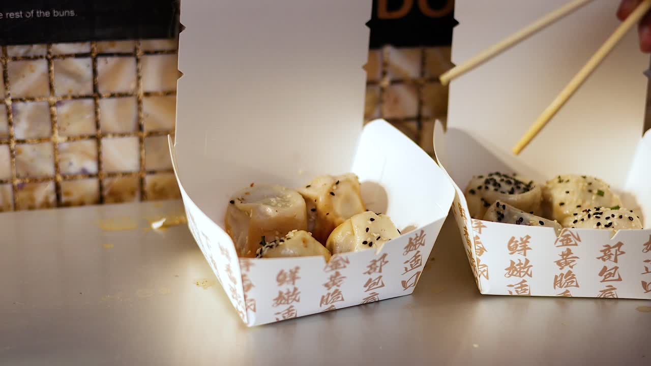 Chopsticks lifting buns from a takeout box