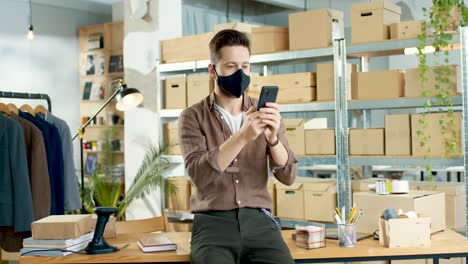 Cucasian-designer-man-texting-on-smartphone-and-leaning-on-the-table-in-a-fashion-clothing-store