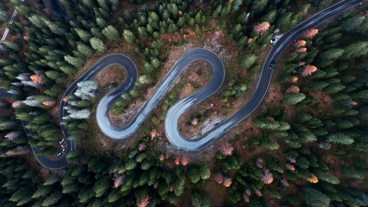 Winding mountain road through dense forest in autumn colors, aerial view from high above