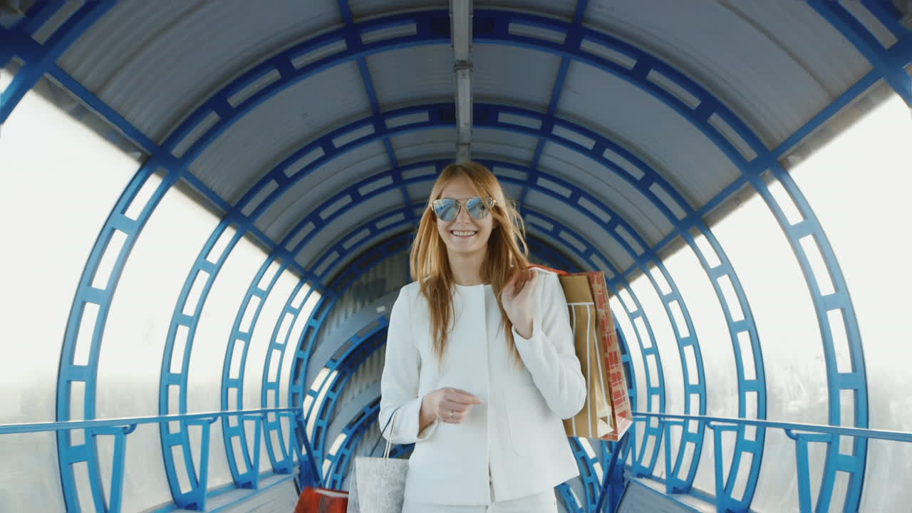 steadicam disparó a una joven elegante con bolsas de compras hablando sobre una transición de vidrio moderna o un túnel