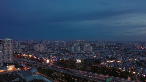 Drone-panning-shot-of-busy-highway-crossing-bridge-and-river-to-large-illuminated-city-at-night