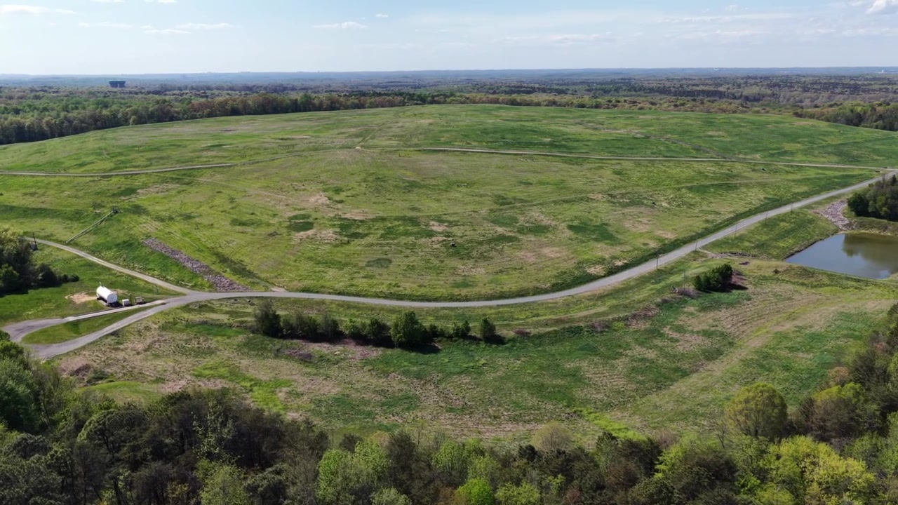 Rozległy wiejski krajobraz rolniczy z krętą polną drogą, zielonymi polami i małym stawem otoczonym drzewami, ukazujący spokojny wiejski krajobraz w Stanach Zjednoczonych wiosną. Szeroki widok z lotu ptaka