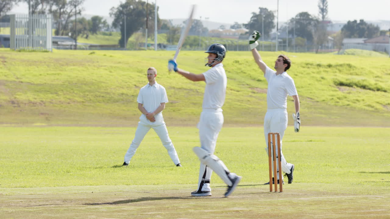 Two teams of male cricket players playing cricket, bowler catching and throwing the ball on pitch