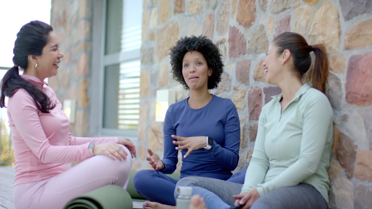 Veninder hygger sig med en livlig snak på terrassen med yogamåtter og smartphone