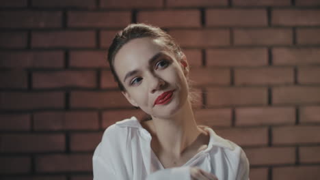 young woman smiling and shyly shruging shoulders on brick wall copyspace