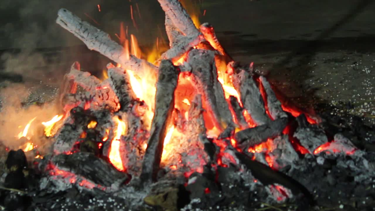 Closeup of glowing campfire burning firewood at night with crackling flames and embers, ideal for nature, survival, relaxation, camping and ambient background scenes.