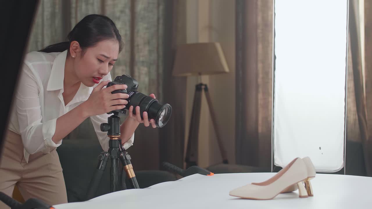 Asian Female Photographer Thinking About Women'S Shoes Position Then Raising Her Index Finger While Taking Photos Of Them In Home Studio