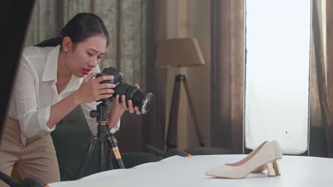 asian female photographer thinking about women's shoes position then raising her index finger while taking photos of them in home studio