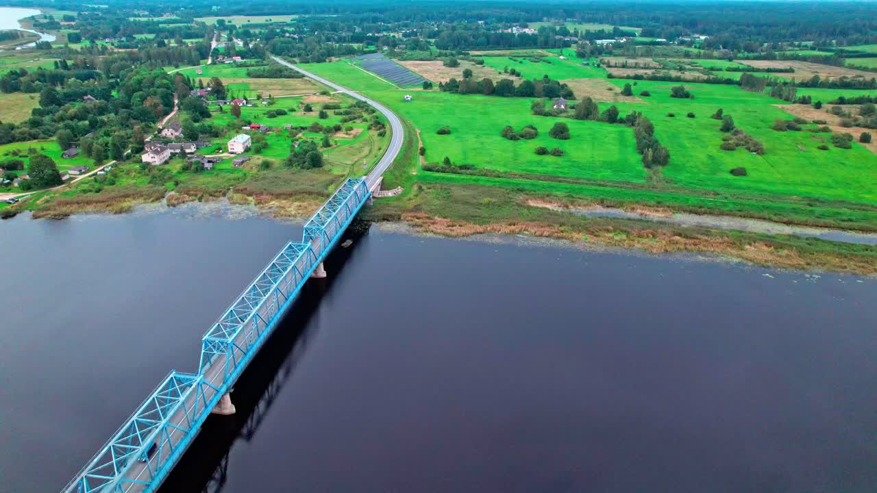 Vast green fields and a blue bridge over the river in Latvia
