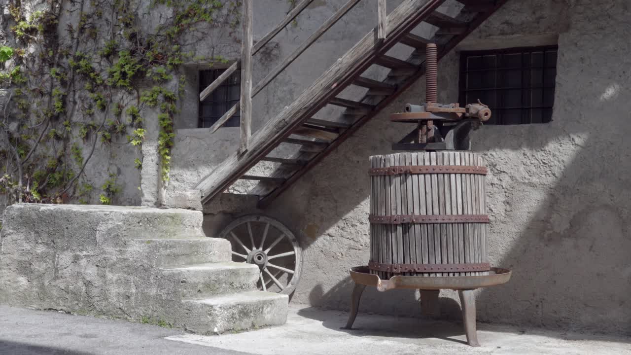 An old grape press stands under a wooden staircase in front of an old building in Kurtinig, Cortina, South Tyrol, Italy