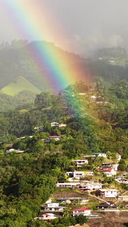 vertical drone shot of real rainbow above hills of tahiti island and papeete, french polynesia